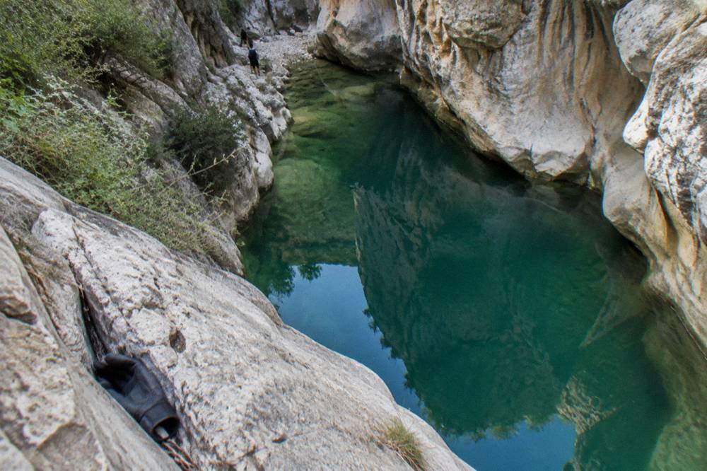 Canyon pool reflecting tall rock walls under open sky at midday