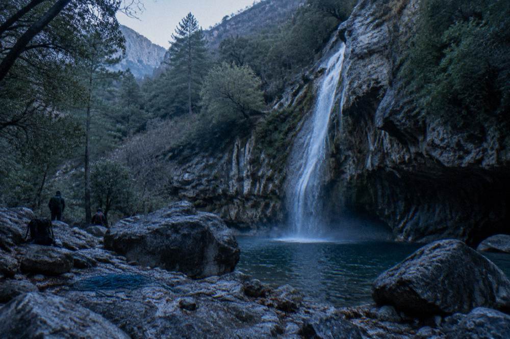 Waterfall dropping through dense green forest into a rocky pool in the Sierra de Santiago